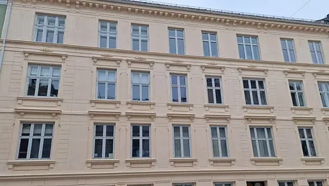 Lys beige bygård i klassisk stil med symmetrisk vindusplassering og utsmykkede fasadedetaljer.