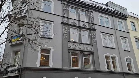Grå bygård med hvite detaljer og utsmykninger rundt vinduene, samt små balkonger.