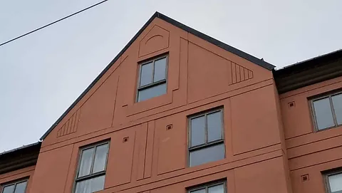 Murbygning i teglfarge med enkle detaljer og vinduer i symmetrisk mønster.
