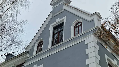 Grå bygård i klassisk stil med hvite gesimser og buede vinduer i øverste etasje.