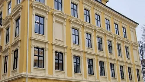 Klassisk hjørnebygning i gul og hvit med store vinduer og dekorative søyler.