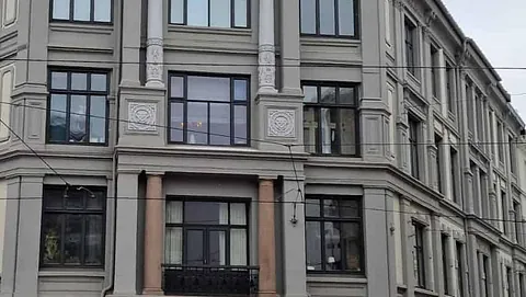 Hjørnebygård i klassisk stil med buede vinduer, søyler og butikker i første etasje.